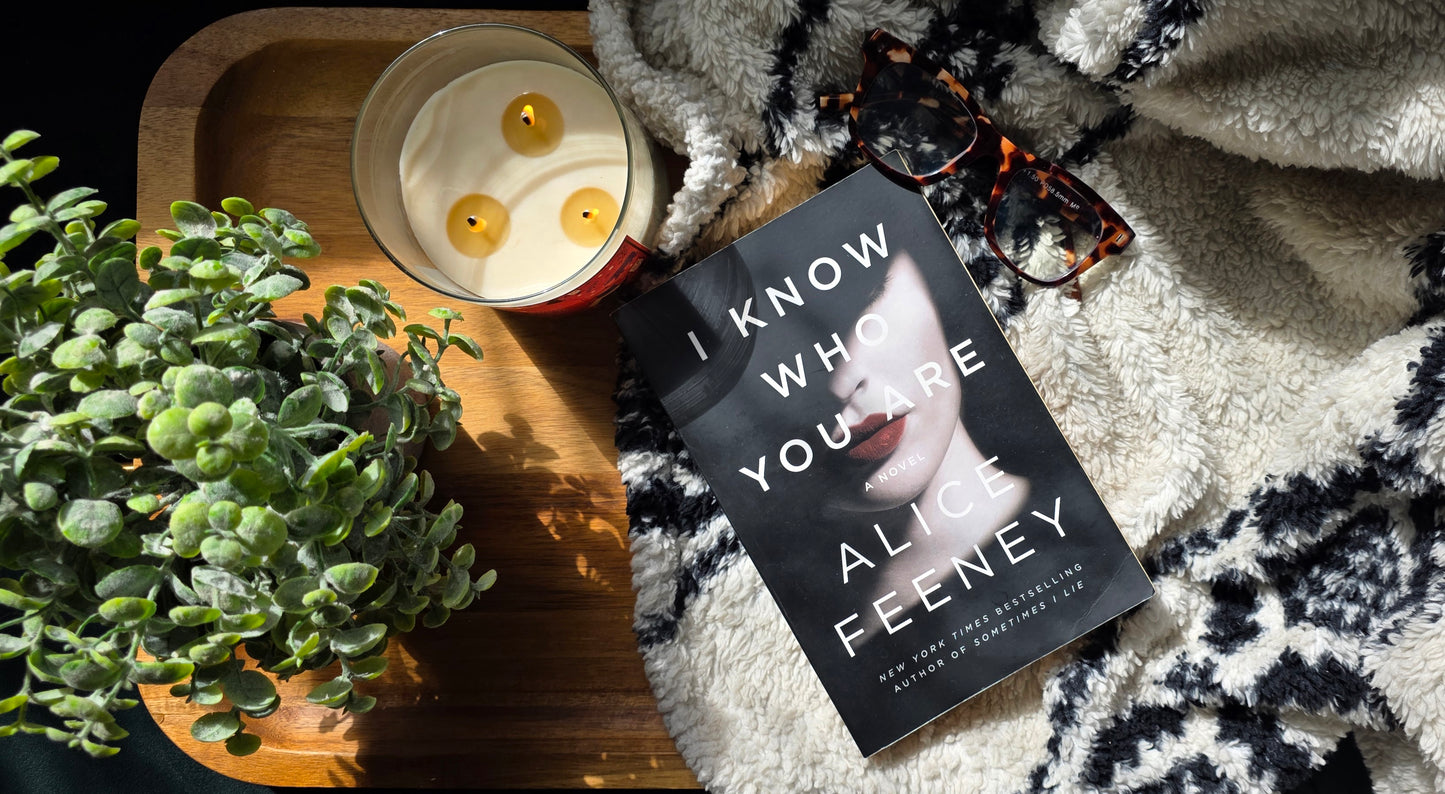 Book titled 'I Know Who You Are' by Ali Feeney on a blanket with a candle and plant in the background.