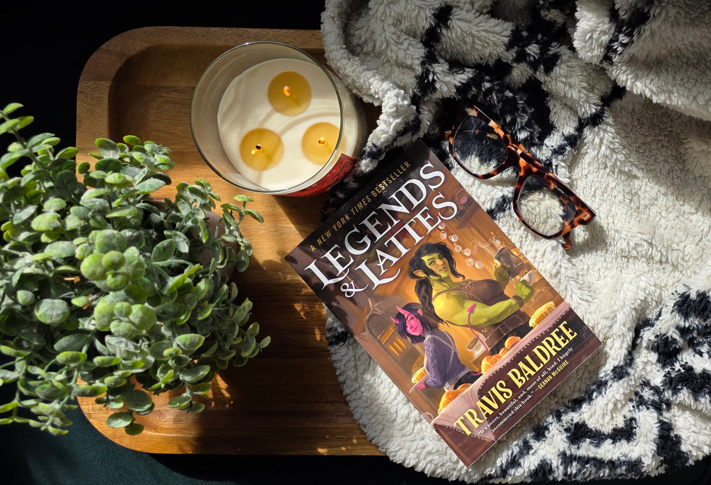 Book titled 'Legends & Lattes' with a candle and glasses on a textured surface.