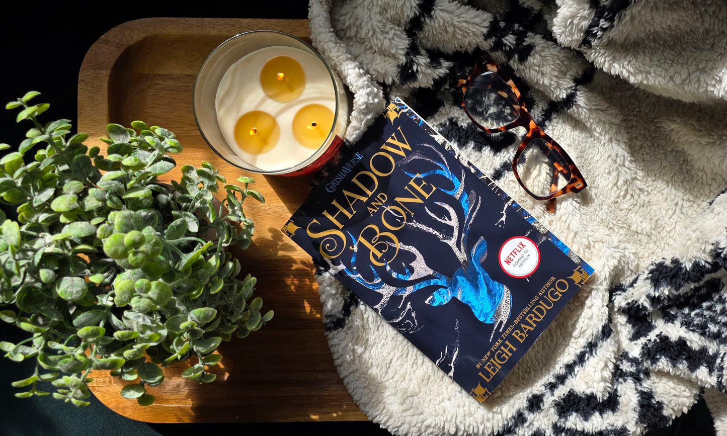 Book 'Shadow and Bone' by Leigh Bardugo on a tray with candles and a plant, on a textured surface.