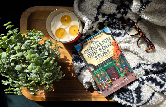 Book titled 'Cinnamon Bun Store' with a candle and plant on a textured surface