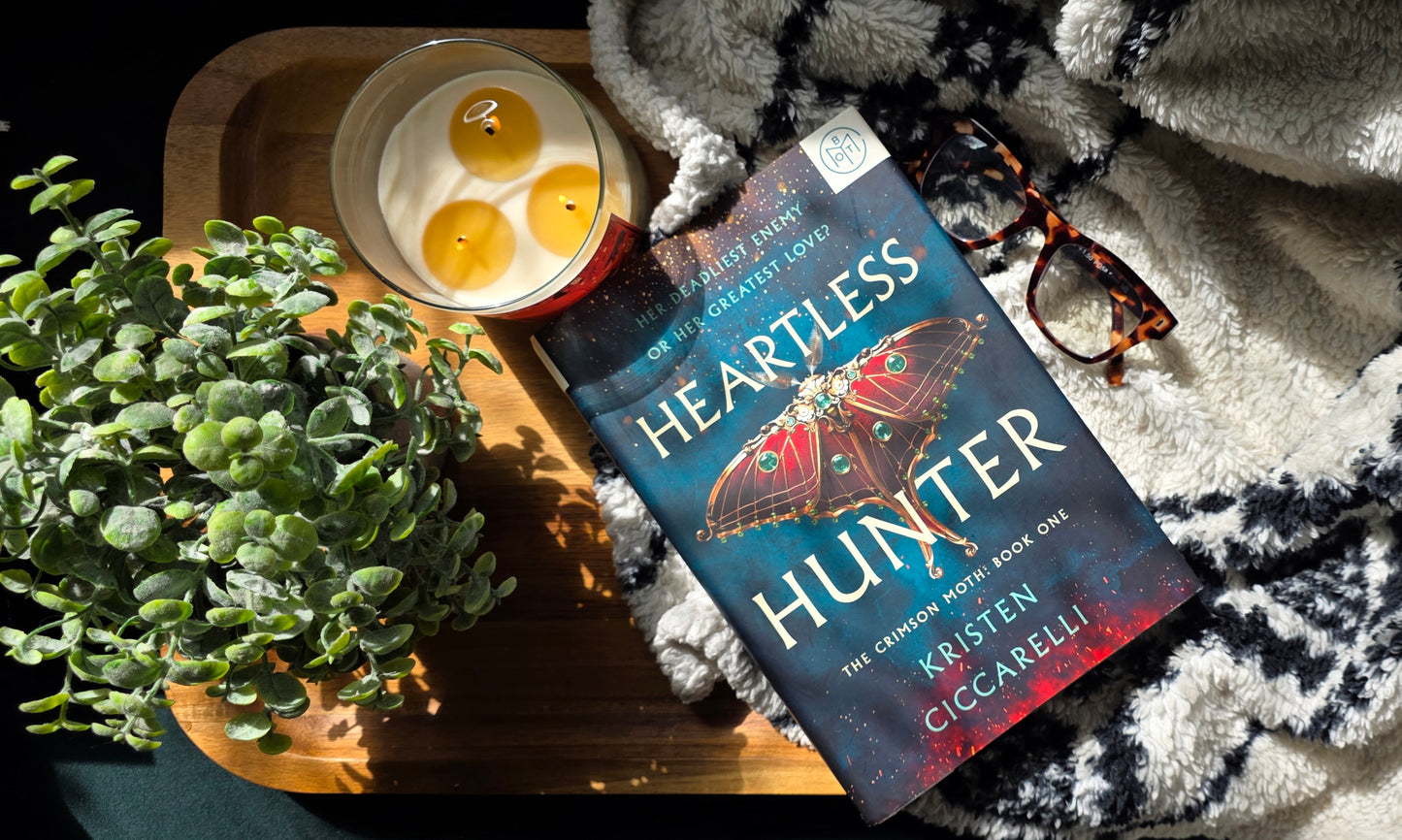 Book titled 'Heartless Hunter' by Kristen L. Coccarel on a tray with a candle and plant