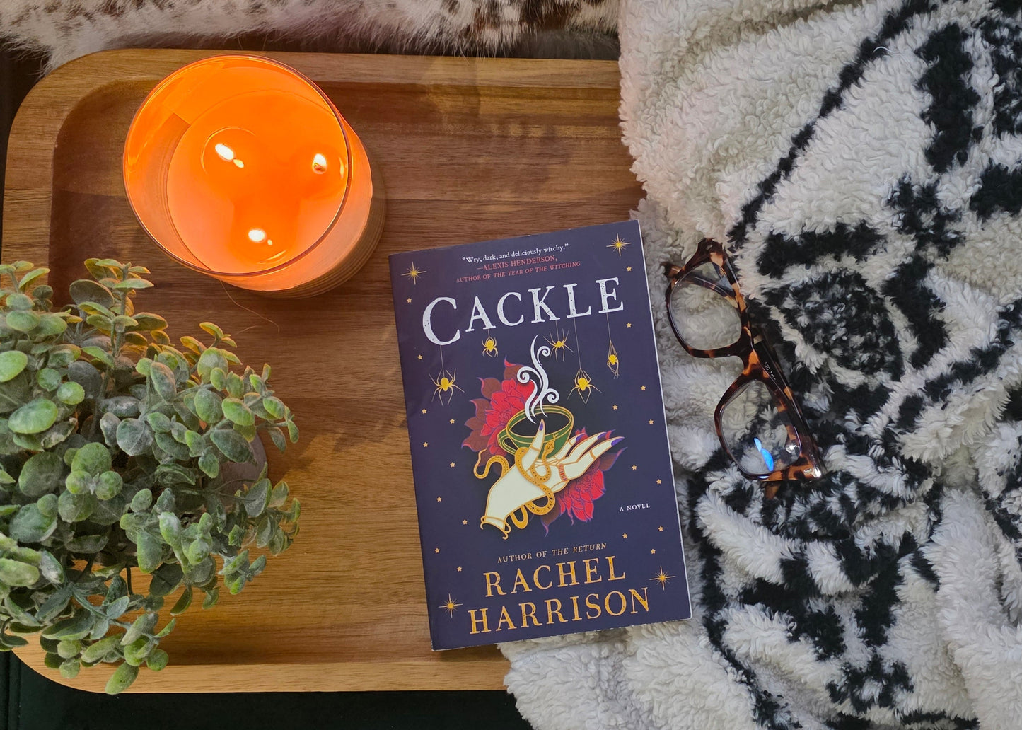 Book titled 'Cackle' by Rachel Harrison on a wooden tray with a candle and decorative items.