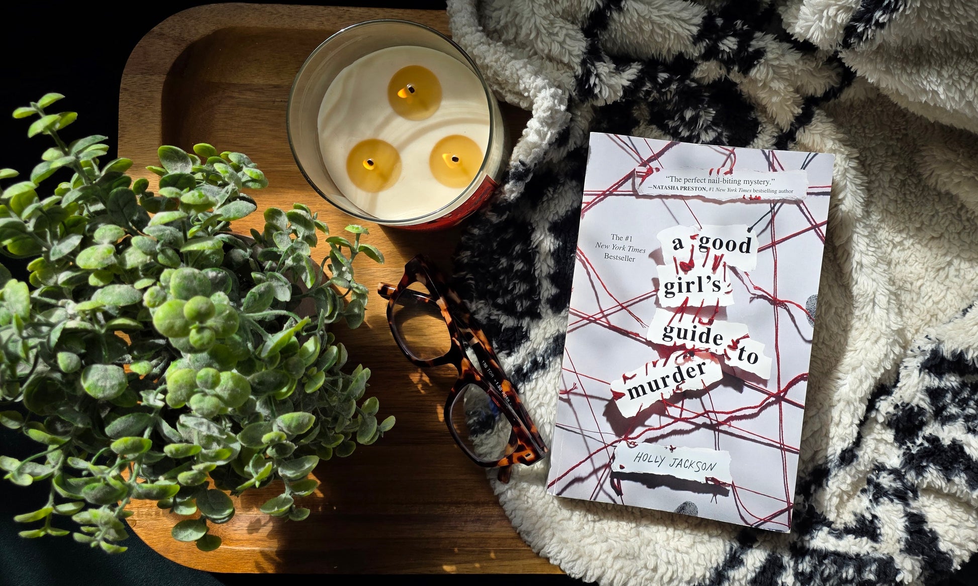 Book titled 'The Murder of the Year' with a candle and plant on a textured surface