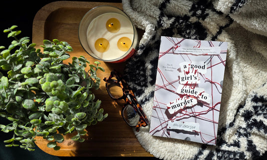 Book titled 'The Murder of the Year' with a candle and plant on a textured surface