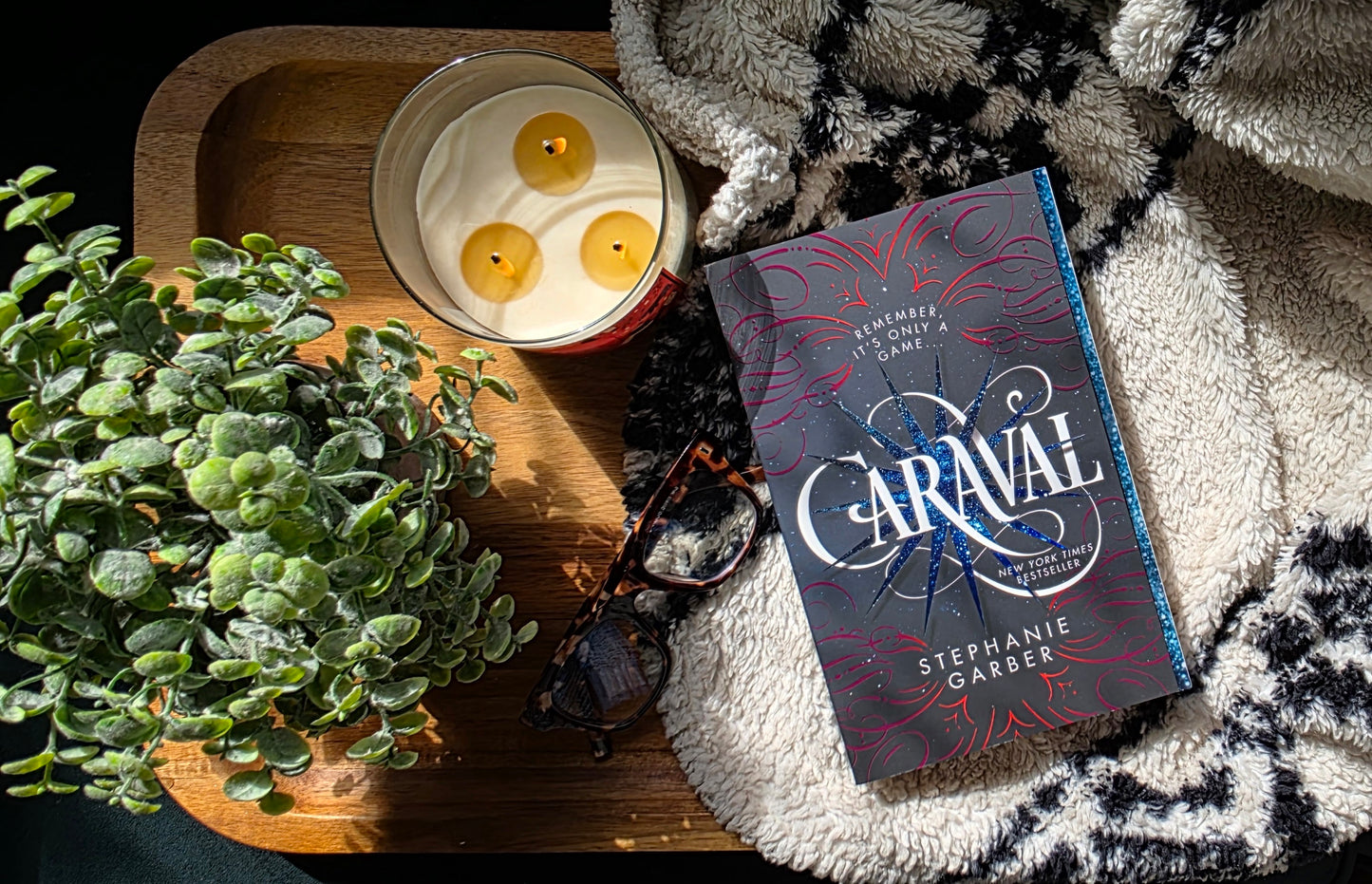 Book titled 'Caraval' by Sarah J. Maas with a candle and plant on a textured surface