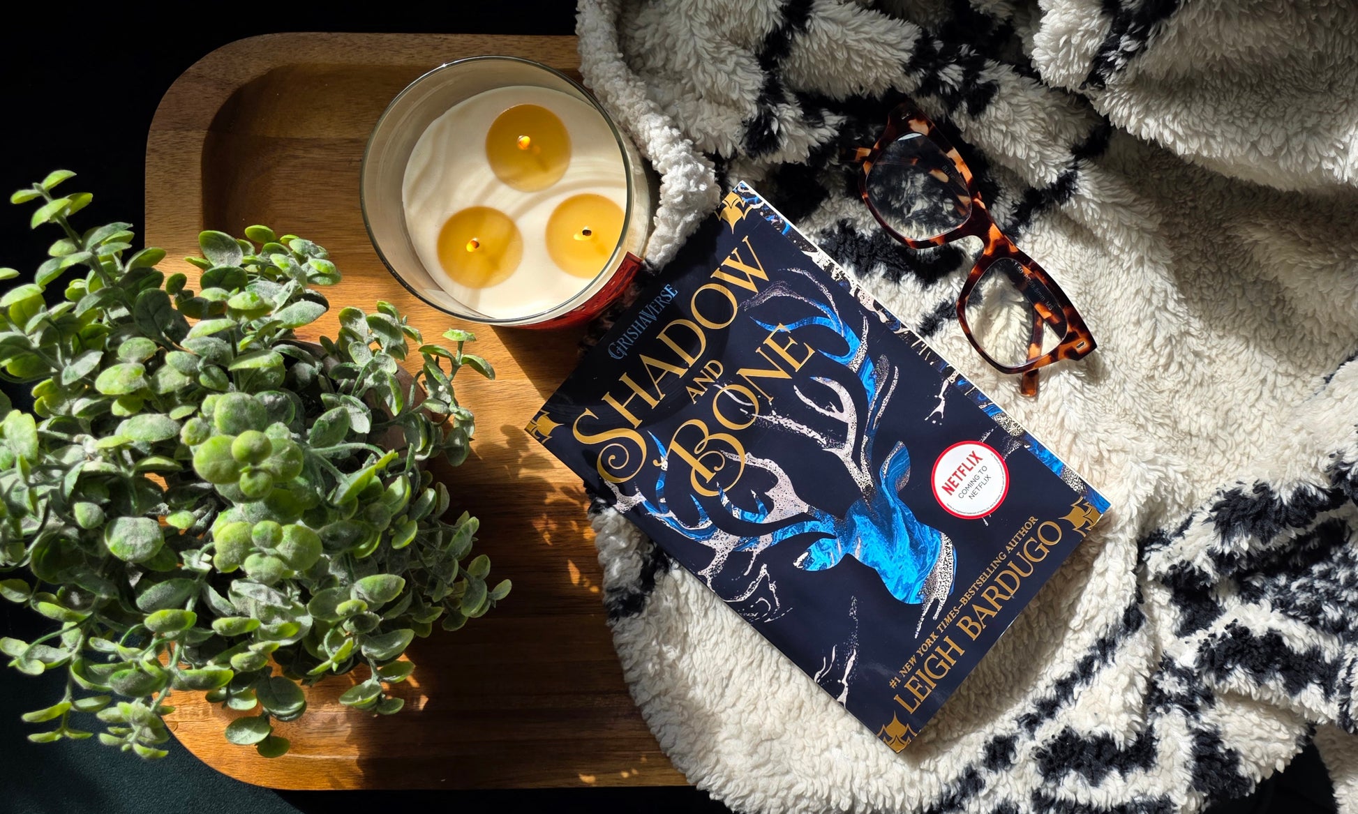 Book 'Shadow and Bone' by Leigh Bardugo on a tray with candles and a plant, on a textured surface.