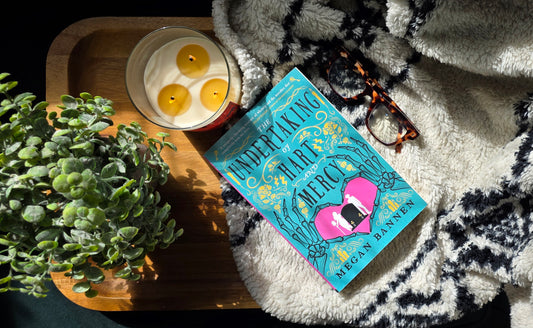 Book titled 'Underaking the Art of Mercy' on a blanket with a candle and plant in the background