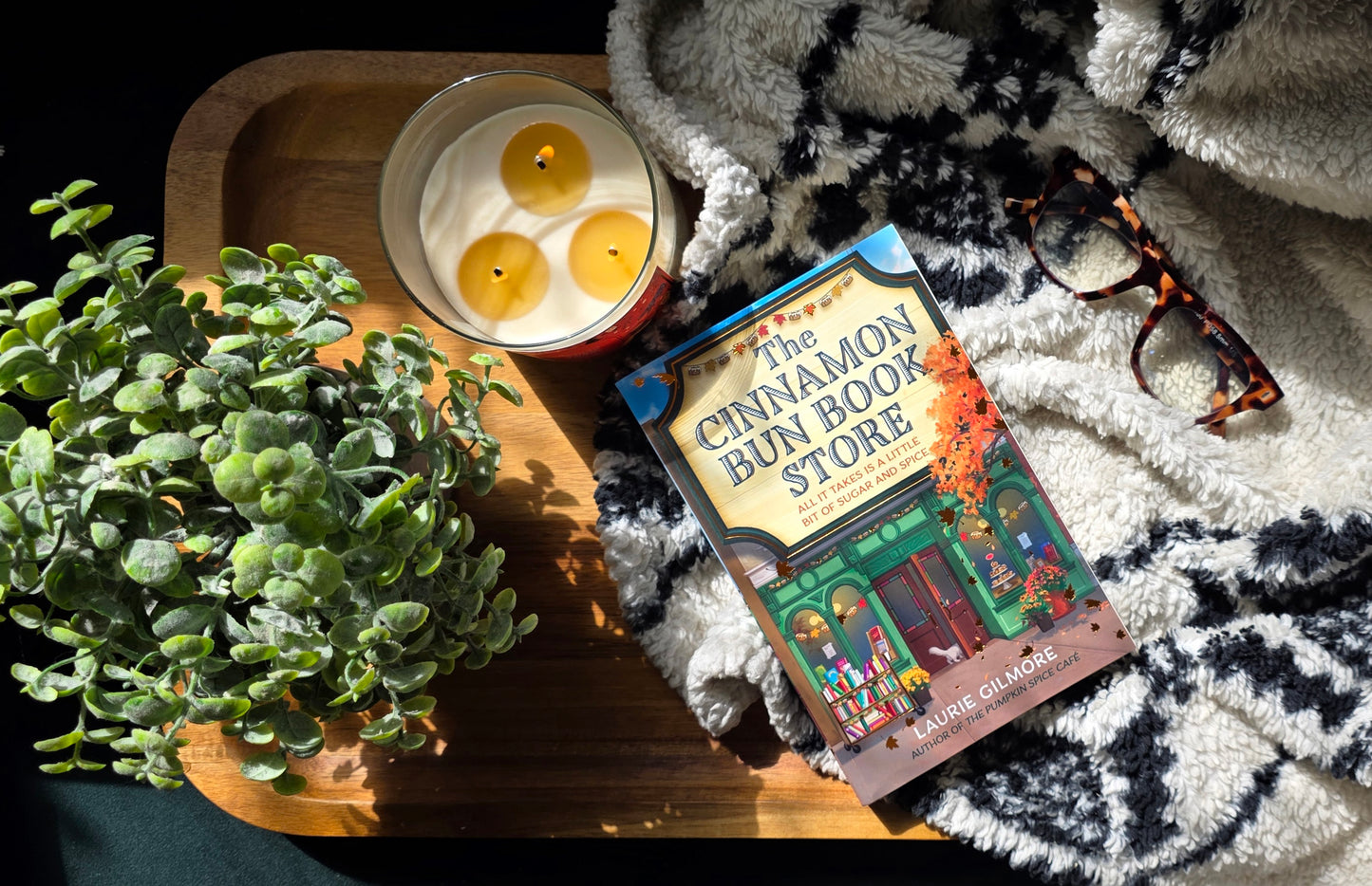 Book titled 'Cinnamon Bun Store' with a candle and plant on a textured surface