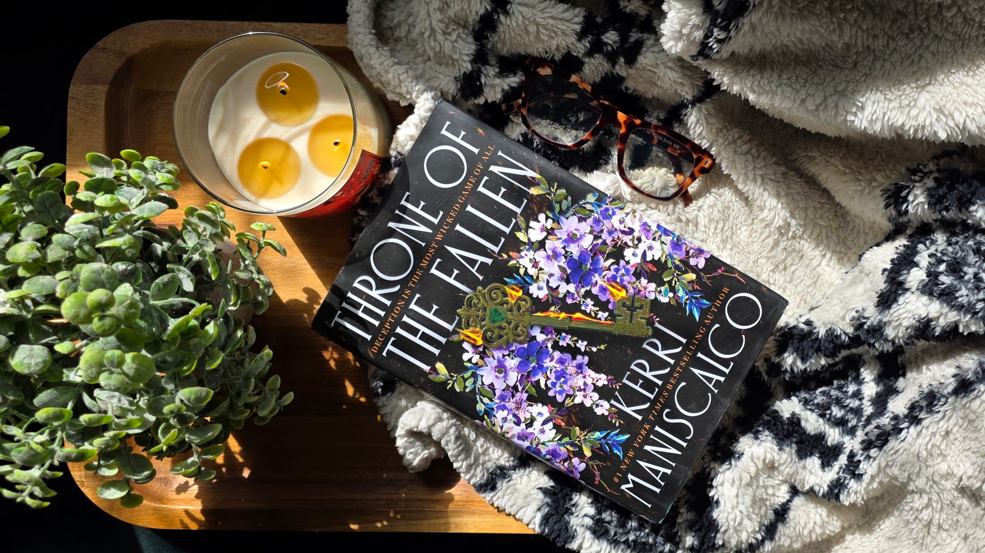 Book titled 'Throne of the Fallen' by Kerri Maniscalco on a cozy surface with candles and plants.
