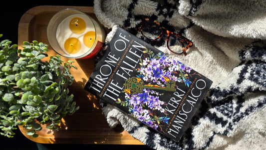 Book titled 'Throne of the Fallen' by Kerri Maniscalco on a cozy surface with candles and plants.