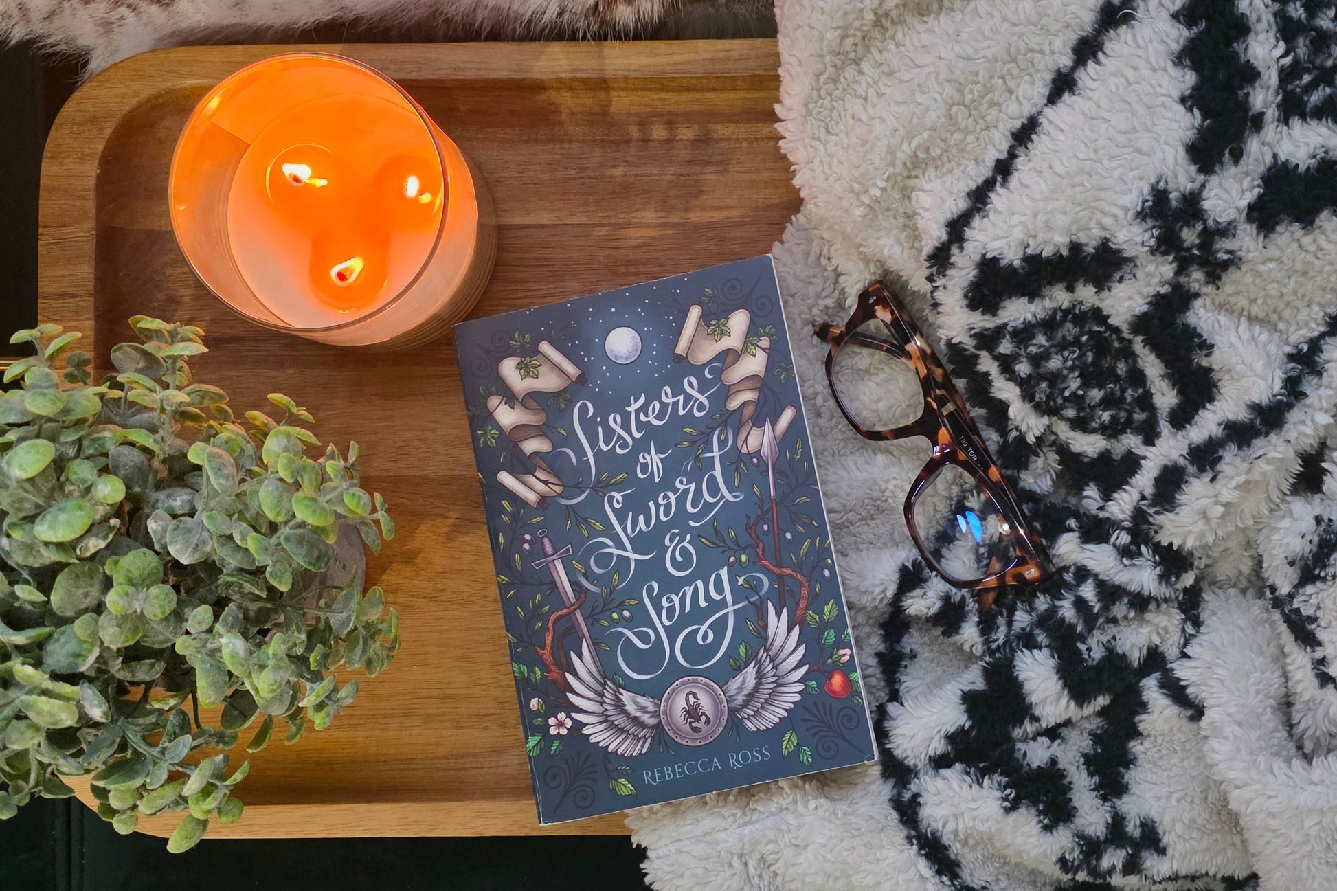 Book titled 'Lover's Lament & Song' on a wooden tray with a candle and plant, on a textured surface.