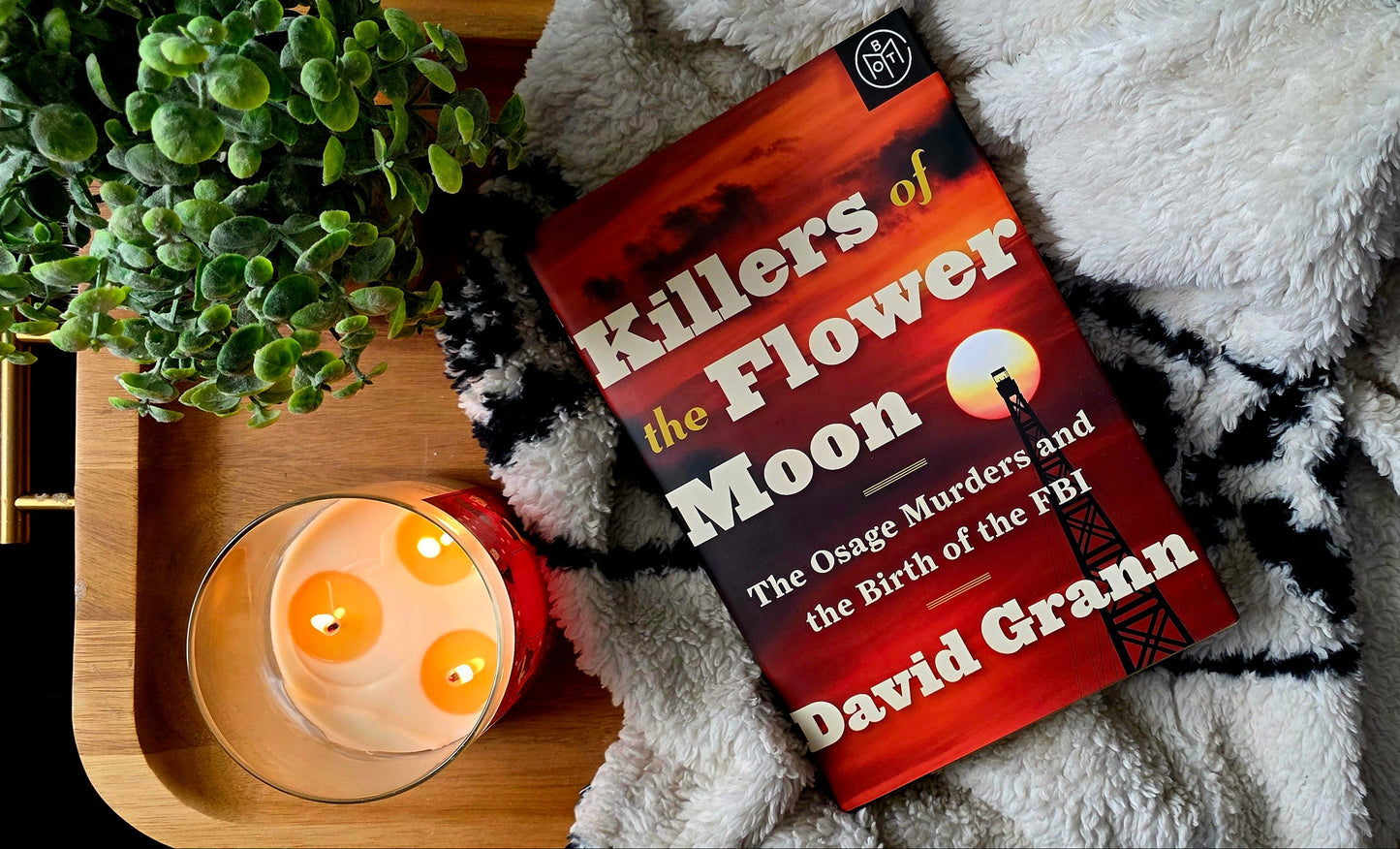 Book titled 'The Flower of the Moon' by David Grann on a tray with a candle and plant.