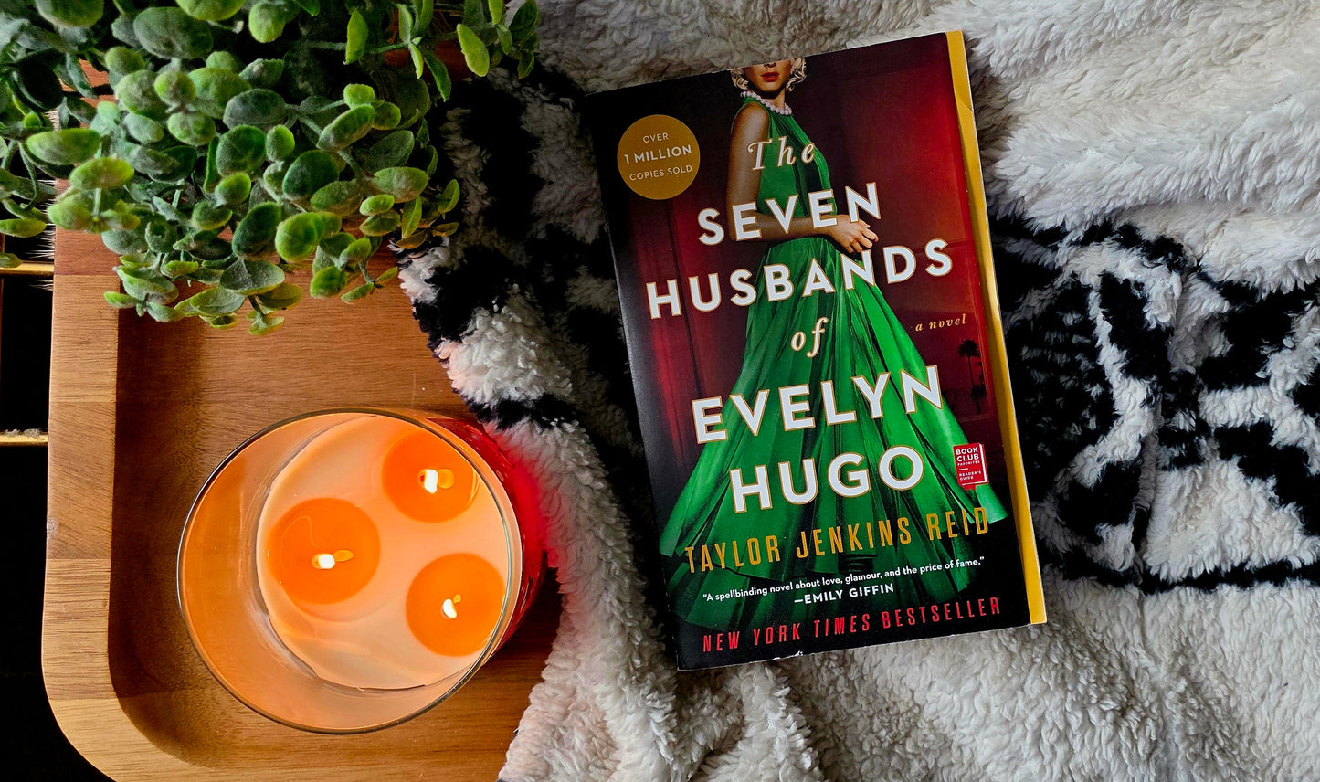 Book titled 'Seven Husbands of Evelyn Hugo' on a textured surface with a candle and plant.