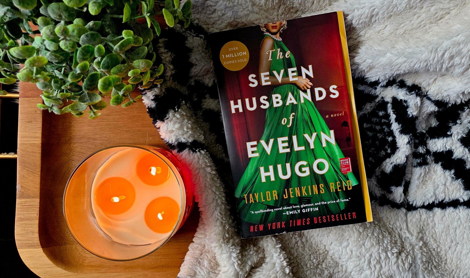 Book titled 'Seven Husbands of Evelyn Hugo' on a textured surface with a candle and plant.