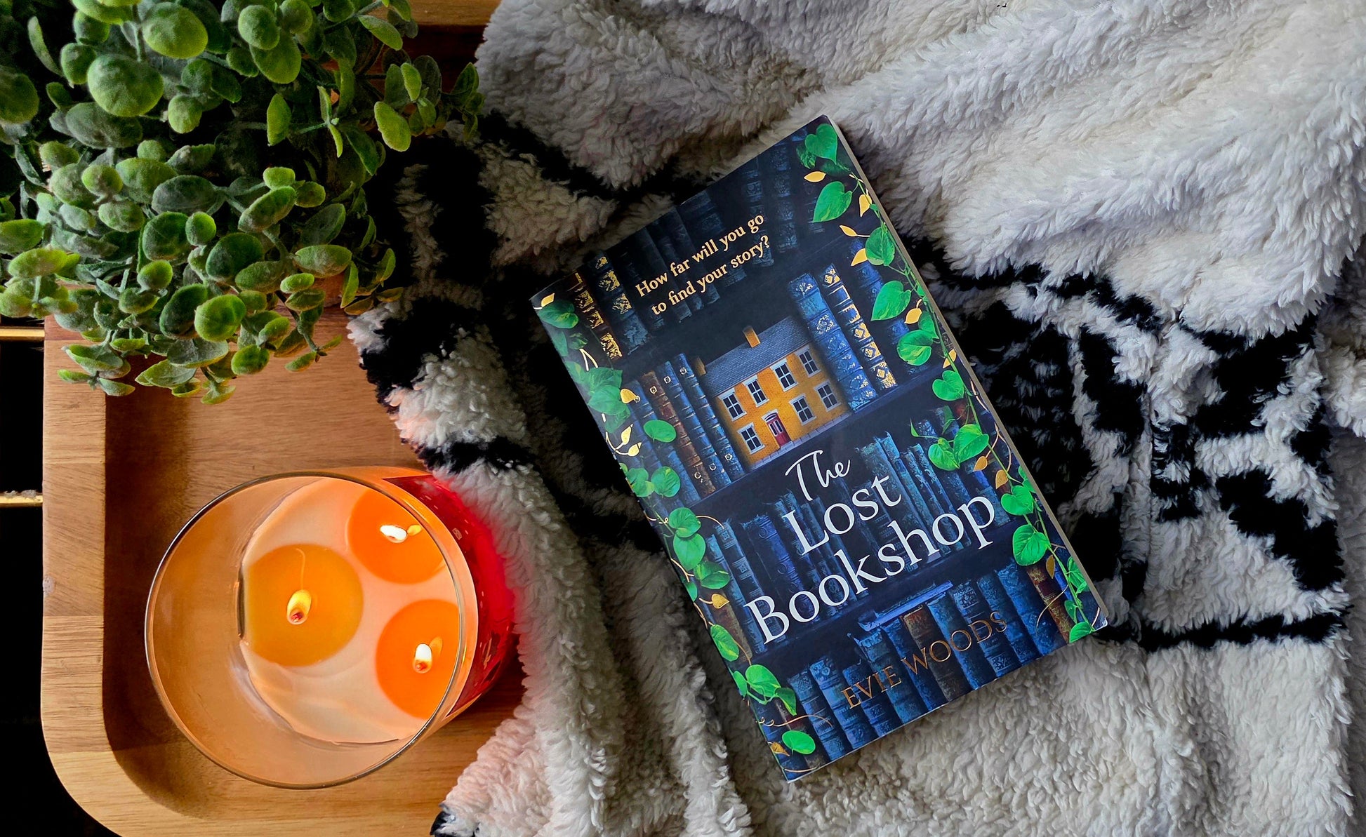 Book titled 'The Lost Bookshop' on a blanket with a candle and plant in the background