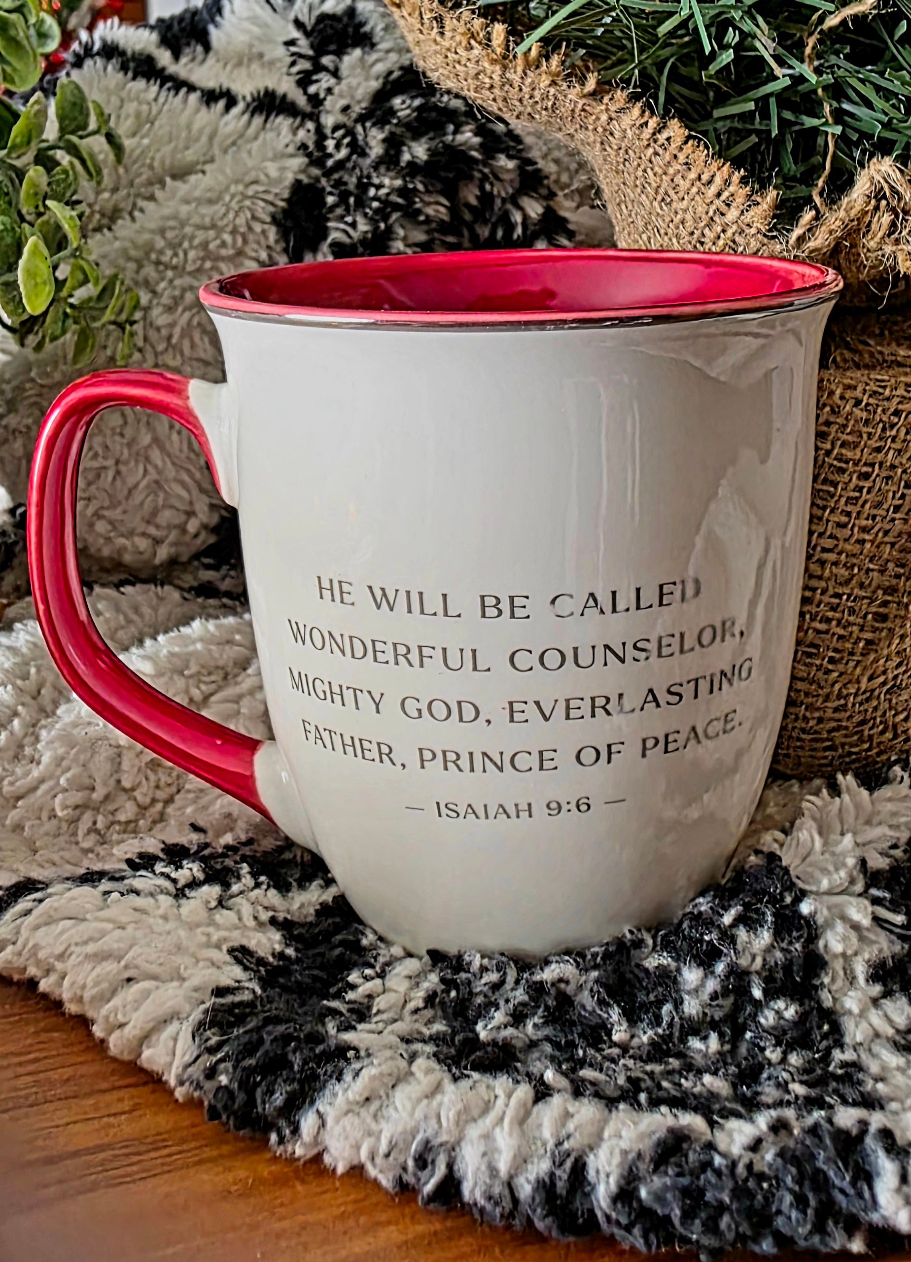 White mug with red handle and interior, featuring a biblical verse, on a textured surface.