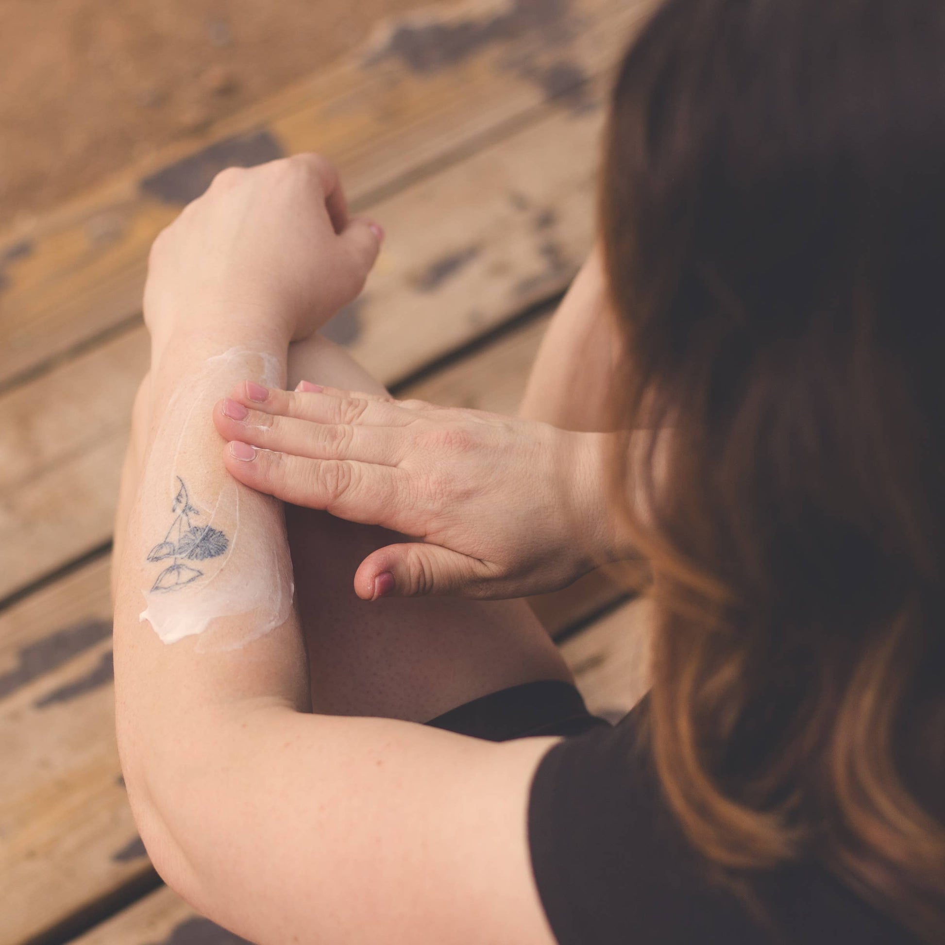 Person with a small tattoo on their arm sitting on a wooden floor.