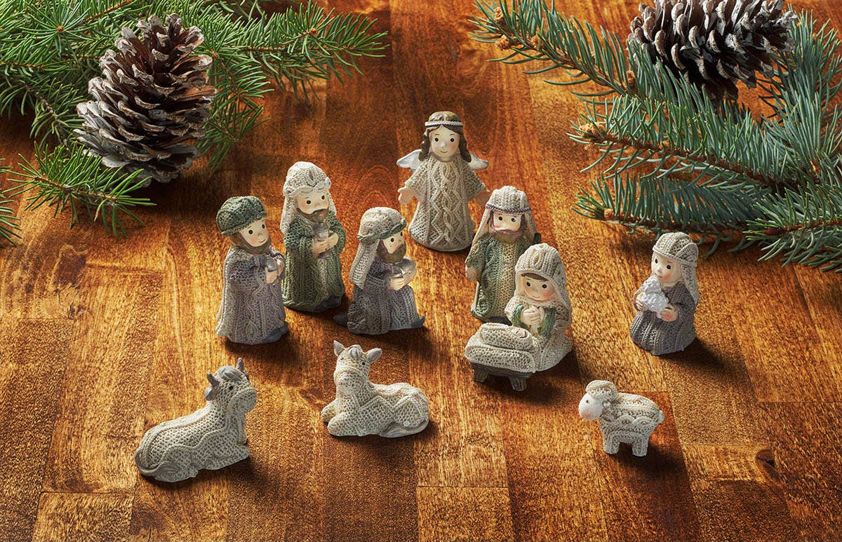 Set of nativity scene figurines on a wooden surface with pine branches and cones.