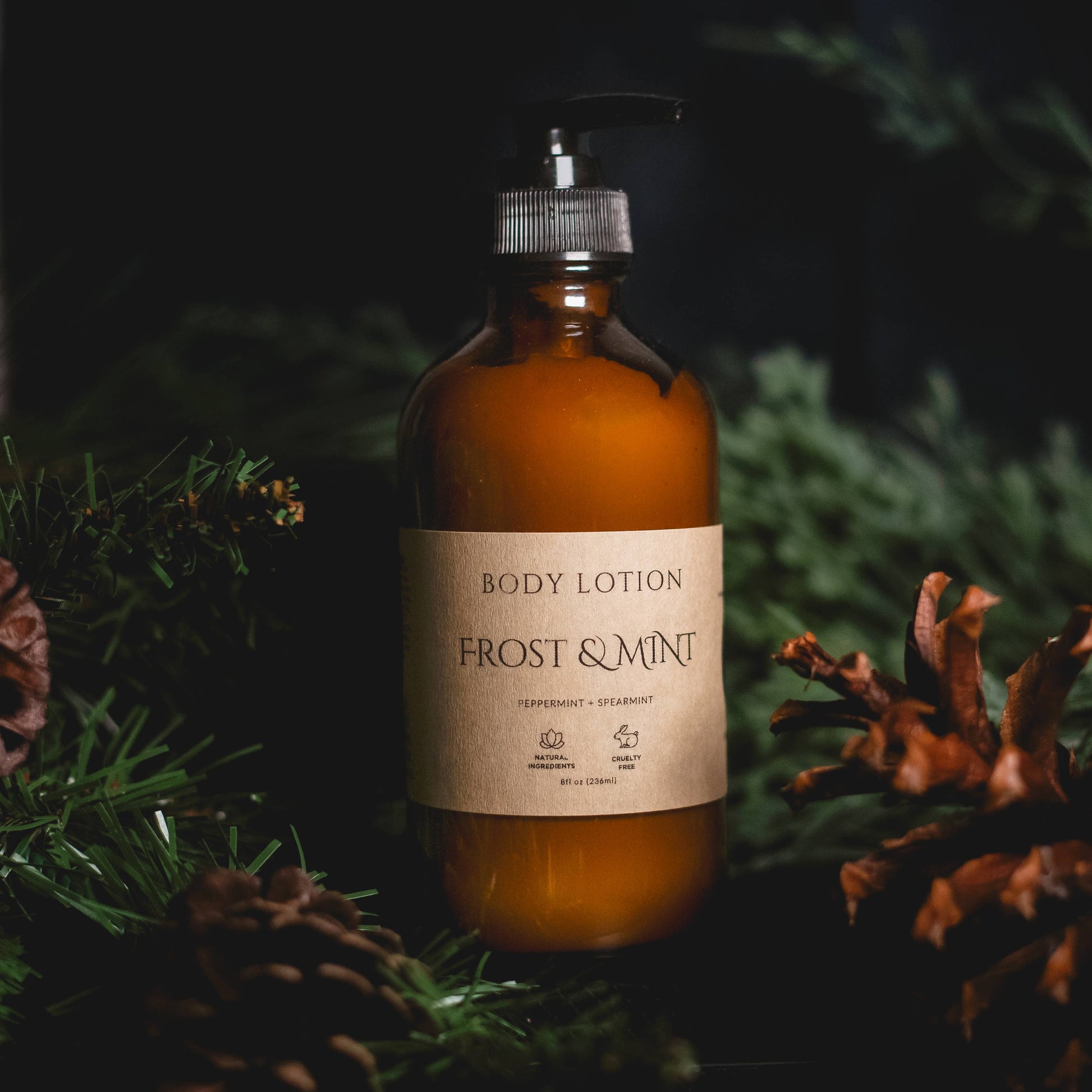Body lotion bottle labeled 'Frost & Mint' surrounded by pine branches and cones.