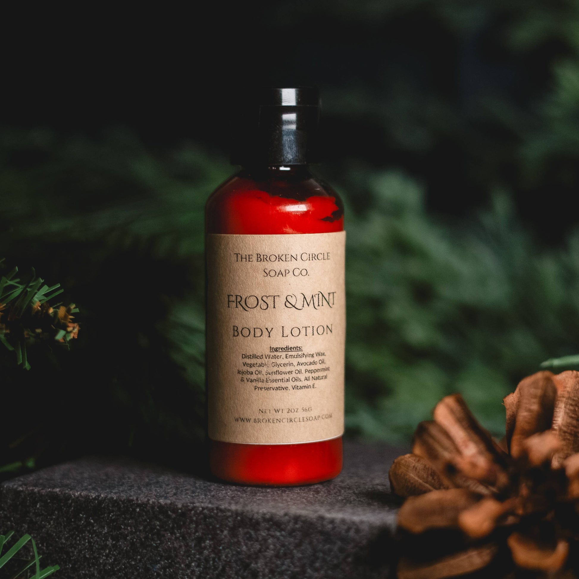 Body lotion bottle with 'Frost & Mint' label on a dark surface with greenery in the background